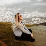 A young woman sits smiling, enjoying a breathtaking view of Jaraguá do Sul, Brazil.